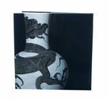 Photo depicts the back of the book, which is void of text and features a close-up image of a white, Chinese vase etched with a black dragon. Background is solid black. 